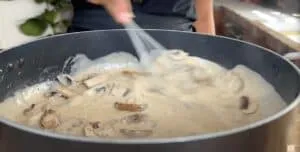 Cooking creamy mushroom sauce in a black pan, stirred with a whisk.