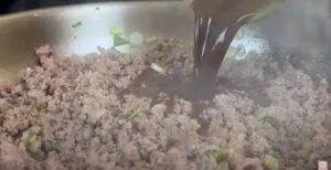 Ground beef and green onions sizzle in a pan as dark sauce is poured in, creating a flavorful meal.