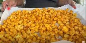 Tray of seasoned diced potatoes on parchment paper, ready for roasting.