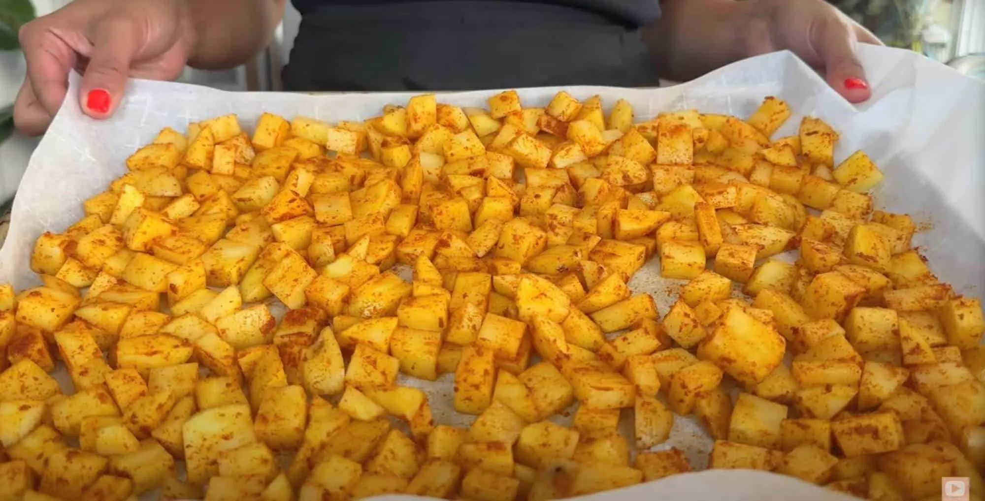 Tray of seasoned diced potatoes on parchment paper, ready for roasting.