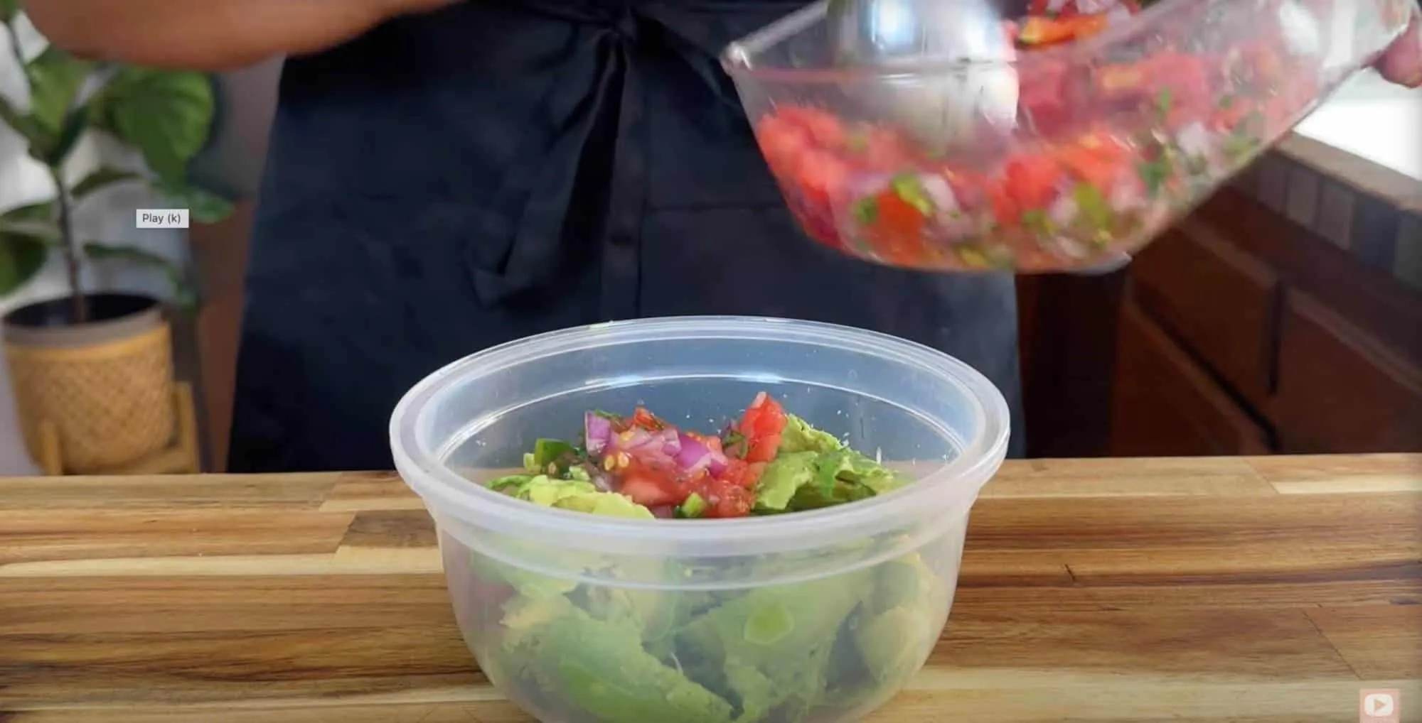 Person making fresh guacamole with avocado, tomato, and onion in a kitchen setting.