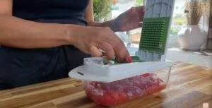 Person using a vegetable chopper to dice onions and tomatoes on a wooden countertop.