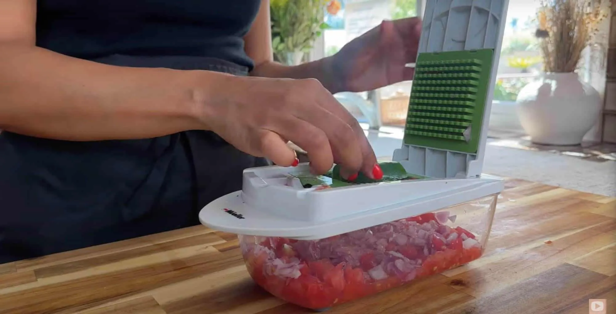 Person using a vegetable chopper to dice onions and tomatoes on a wooden countertop.