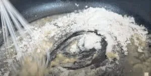 Whisking flour and butter in a pan to make a roux for sauce preparation.