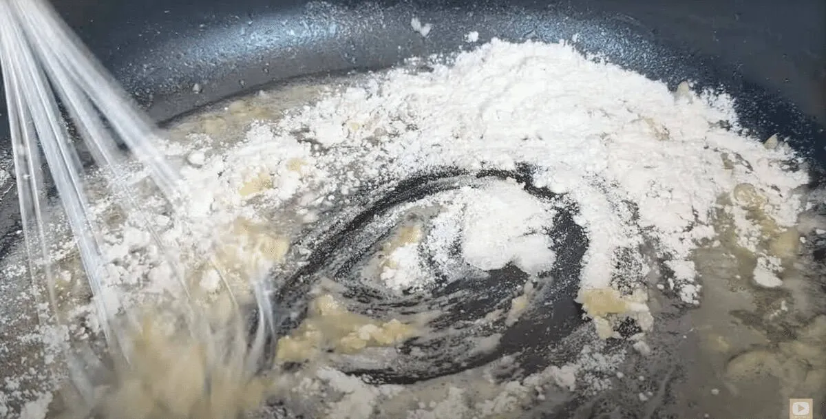 Whisking flour and butter in a pan to make a roux for sauce preparation.