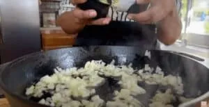 Chopped onions sautéing in a cast iron skillet on a kitchen stove.