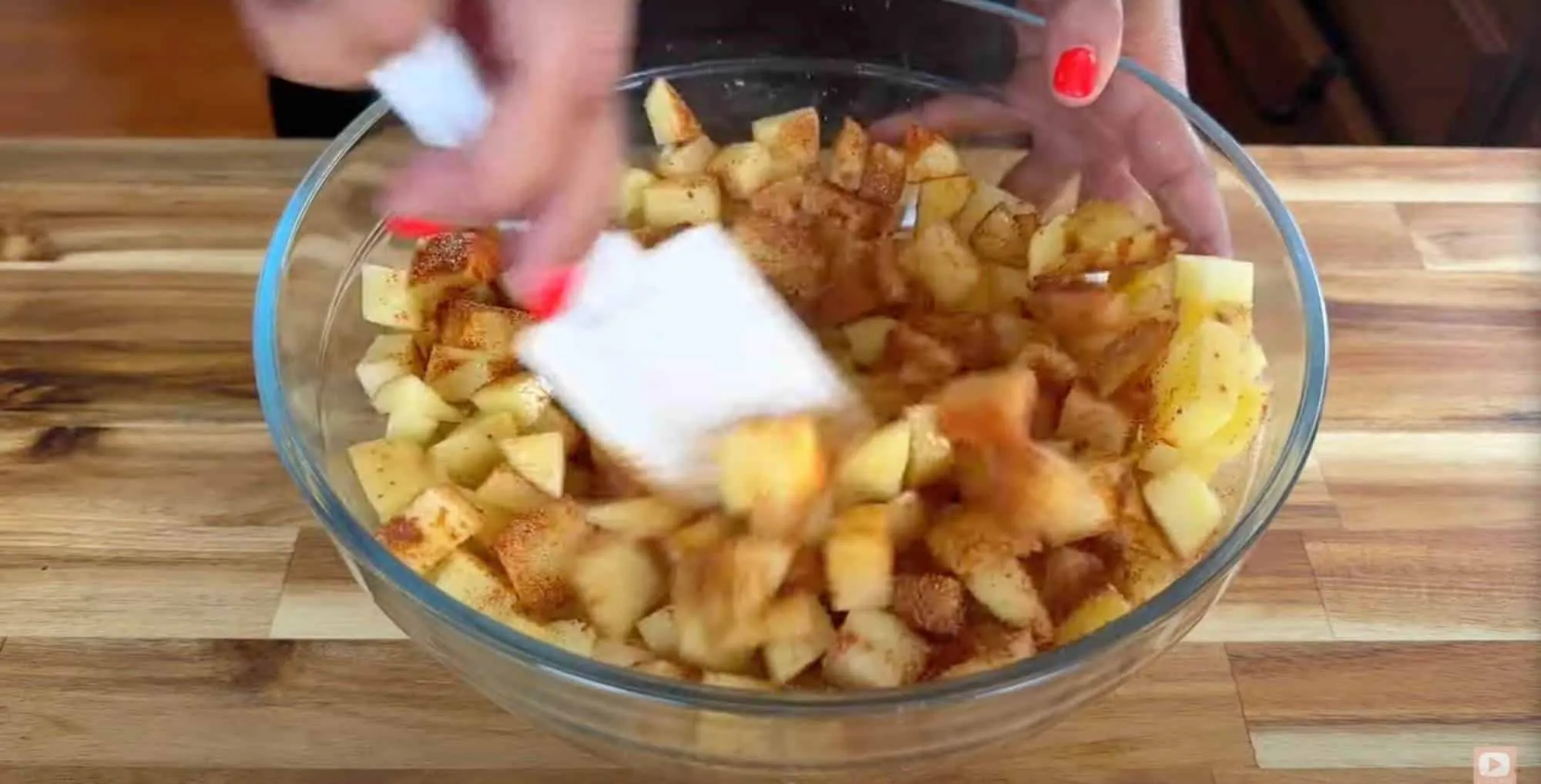 Mixing diced apples with cinnamon in a glass bowl for pie preparation.