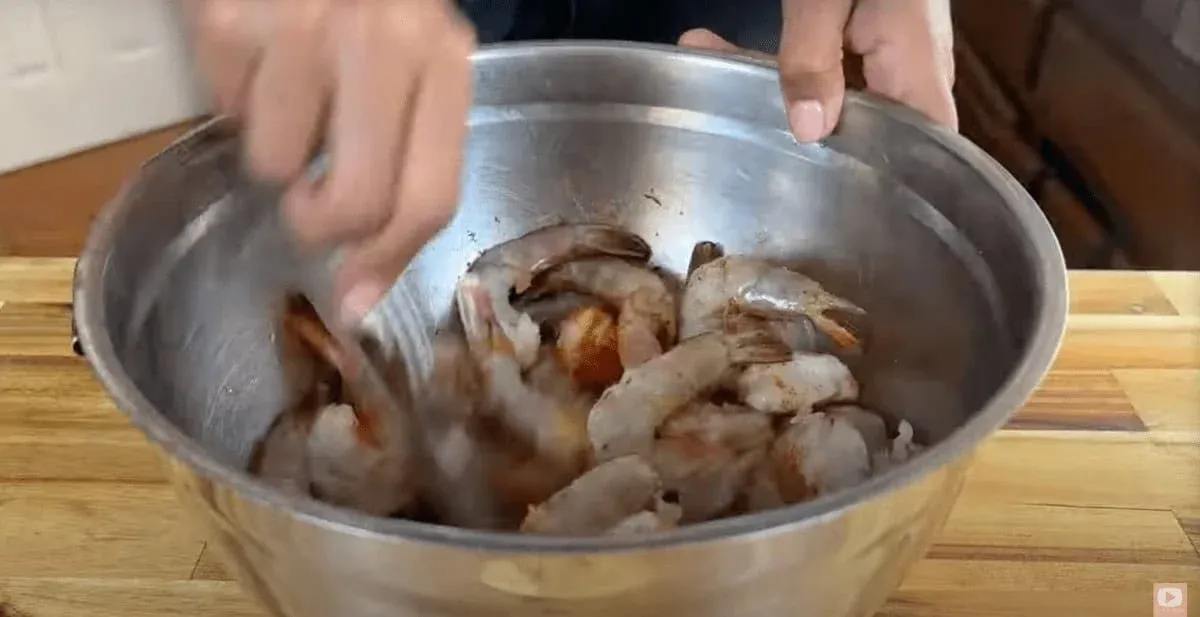 Person mixing peri peri shrimp with spices in a stainless steel bowl on a wooden countertop. Perfect for seafood recipes.