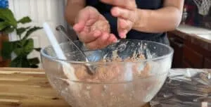 Person shaping meatballs over a mixing bowl on a wooden countertop.