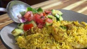 Plate of spiced rice with chicken and fresh salad being served with a spoon, showcasing a colorful and appetizing meal.