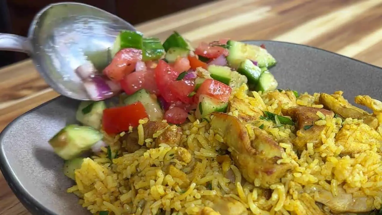 Plate of spiced rice with chicken and fresh salad being served with a spoon.