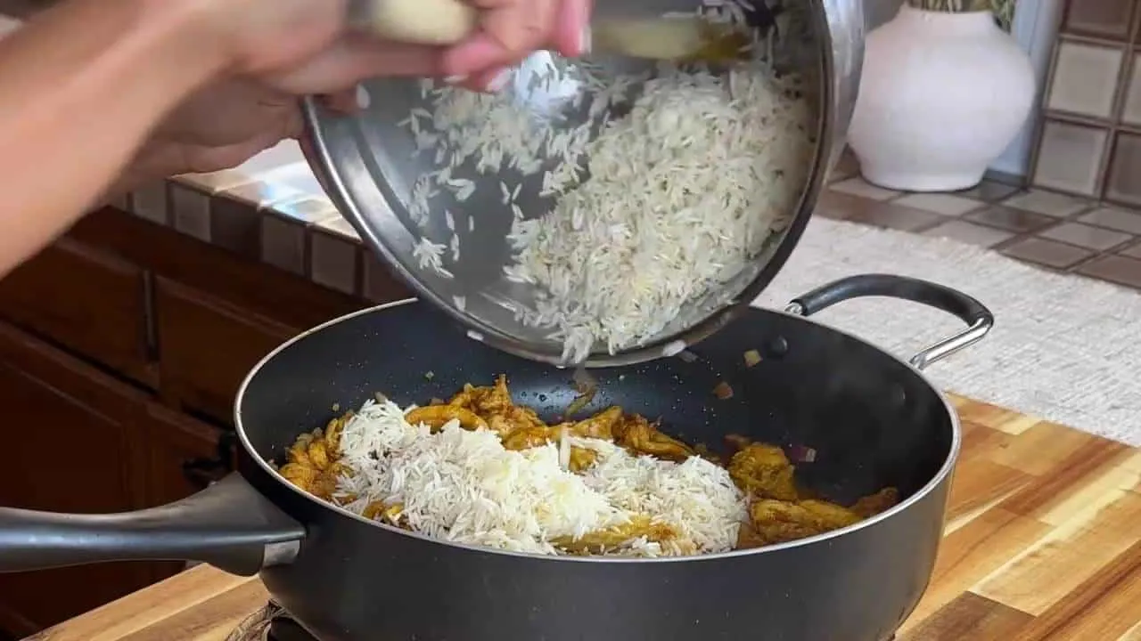 Adding basmati rice to a pot of spiced chicken on a kitchen counter.