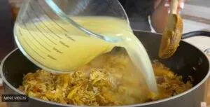 Pouring broth into a pan with rice and chicken for a flavorful homemade dish.