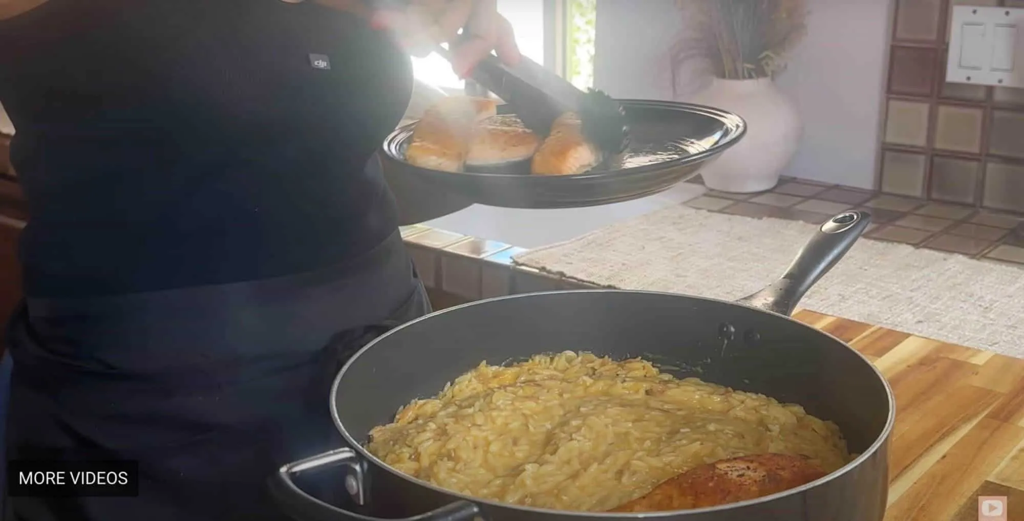 Chef plating grilled salmon over creamy orzo in a kitchen setting.