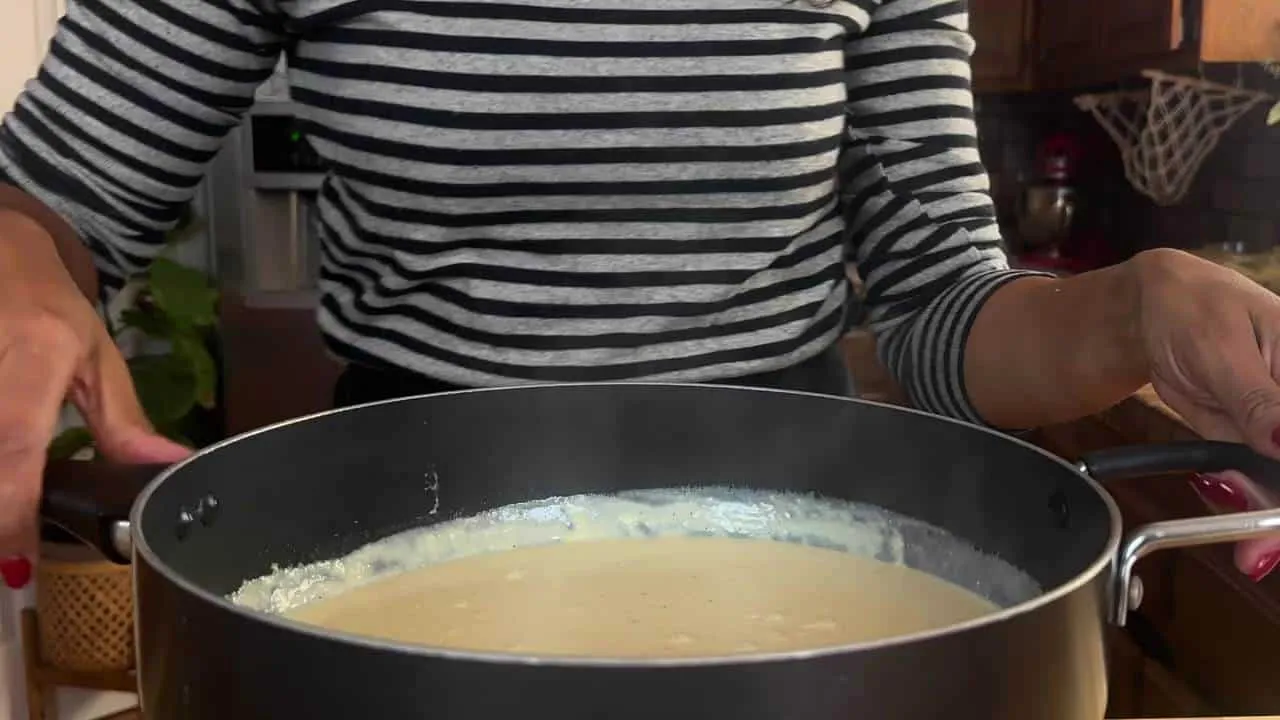 Person stirring creamy sauce in a pot in a cozy kitchen setting.