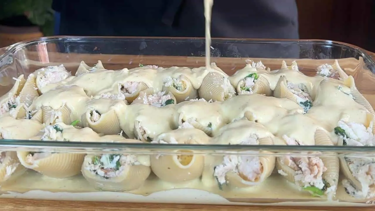 Cheesy stuffed pasta shells in a glass dish, covered with creamy sauce, ready for baking. Perfect Italian comfort food.