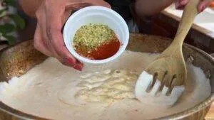 Adding spices to creamy sauce with wooden spoon in pan for a delicious recipe. Perfect for rich flavor enhancement.