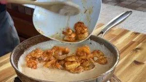 Cooked shrimp being poured into a creamy sauce in a skillet for a flavorful seafood dish.