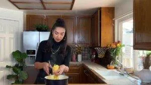 Woman cooking pasta in a cozy kitchen with wooden cabinets and bright flowers on the counter.