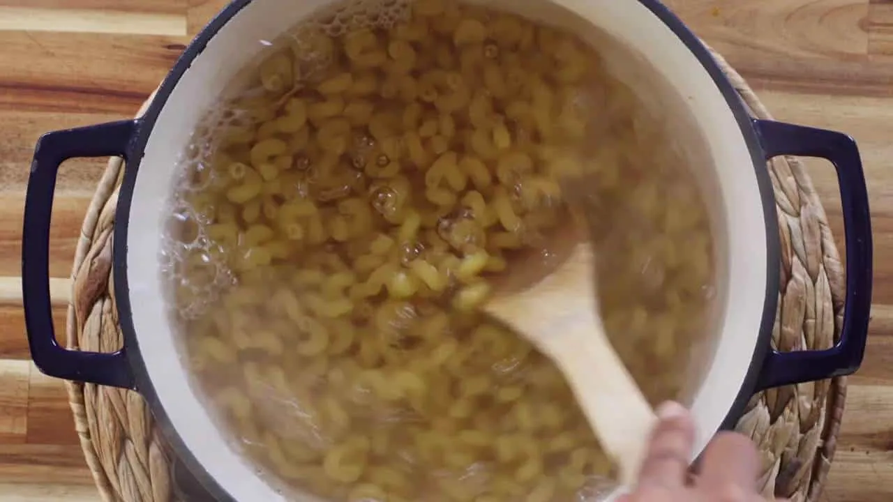 Boiling cavatappi pasta in a pot with a wooden spoon stirring, on a wooden table.