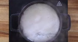 Pot of milk boiling on a stovetop, creating steam, viewed from above.