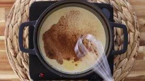 Creamy rice pudding with cinnamon being stirred in a pot on a stove.