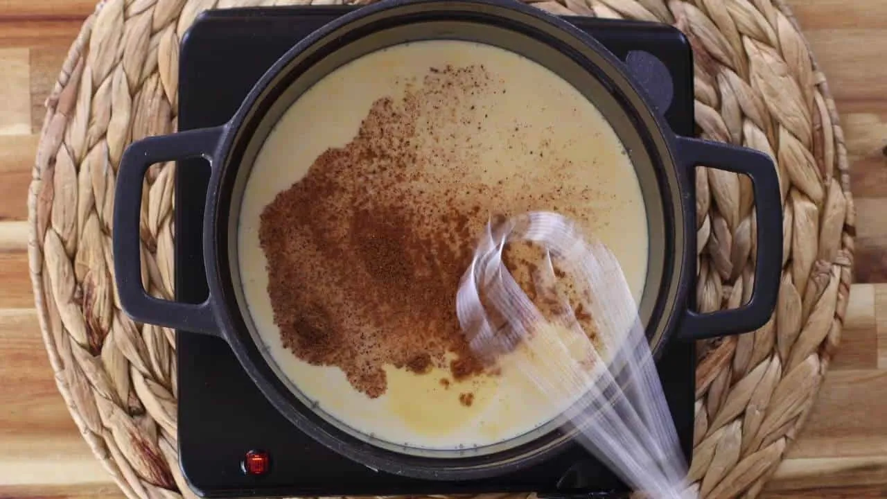 Creamy rice pudding with cinnamon being stirred in a pot on a stove.