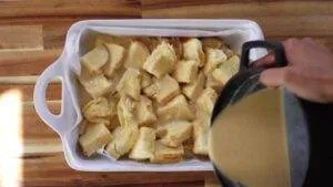 Pouring custard over bread cubes for homemade bread pudding in a white dish, ready for baking.