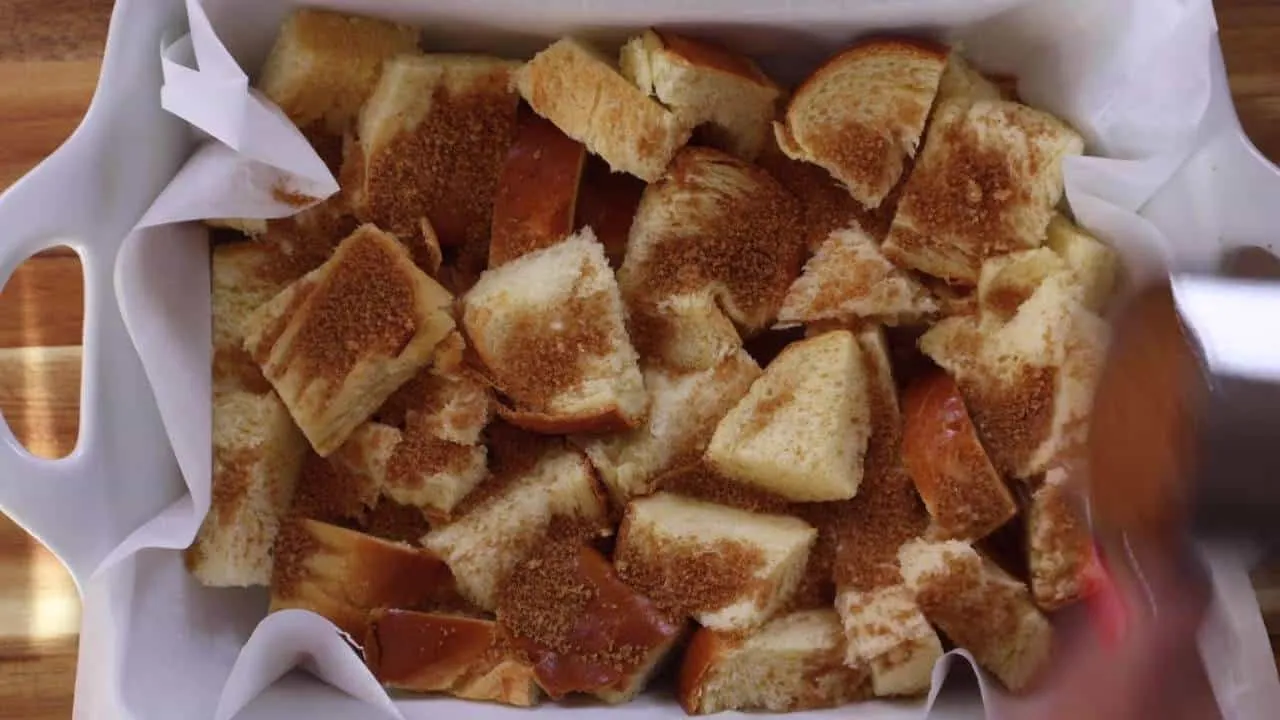 Challah bread topped with brown sugar in a baking dish, ready to be baked for dessert.