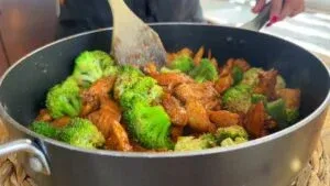 Cooking delicious chicken and broccoli stir-fry in a pan with wooden spatula. Healthy dinner preparation.