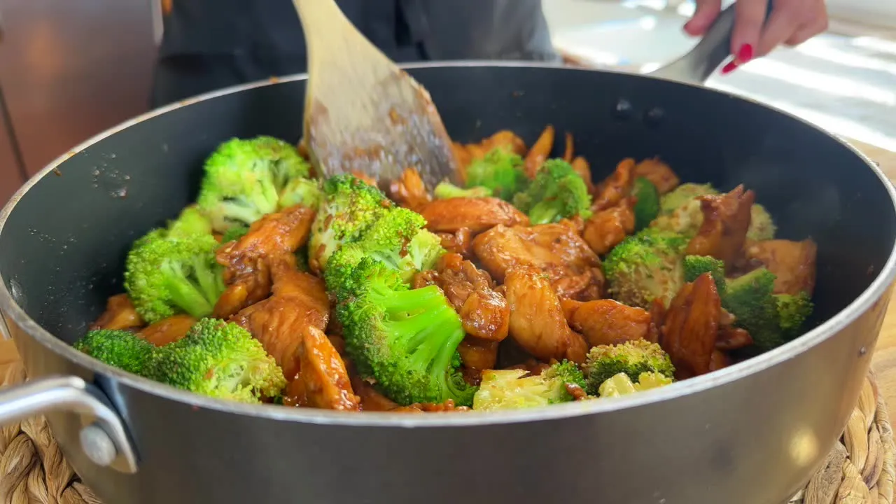 Cooking delicious chicken and broccoli stir-fry in a pan with wooden spatula. Healthy dinner preparation.