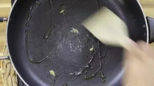 Stirring garlic in a frying pan with oil on a wooden spatula for cooking preparation.