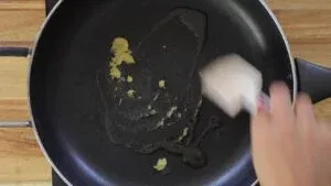 Stirring garlic and ginger in a hot pan with oil on a wooden countertop cooking scene.