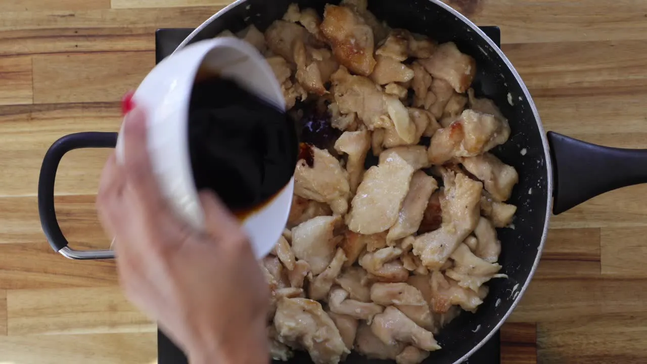 Pouring sauce over cooked chicken pieces in a frying pan for a savory meal preparation.