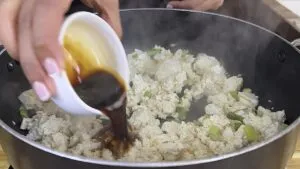 Pouring soy sauce into a pan with tofu and green onions for a delicious meal.