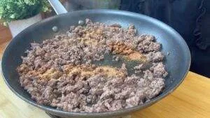 Cooking seasoned ground beef in a skillet with a sprinkle of spices.