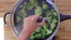 Broccoli in a steaming pot on a wooden kitchen countertop. Healthy cooking preparation.