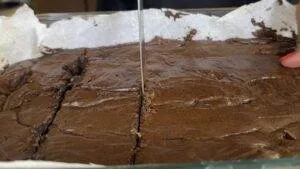 Cutting fresh, homemade brownies on parchment paper in a glass baking dish.