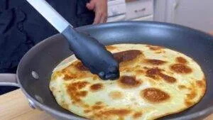 Cooking golden brown quesadilla in pan with tongs in kitchen setting.