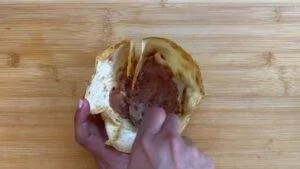 Scooping chocolate out of a cocoa pod with hands on a bamboo cutting board.