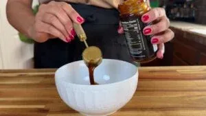 Person pours sauce from jar into white bowl on wooden counter.