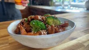Stir-fried chicken with broccoli and sesame seeds in a bowl on a wooden counter.