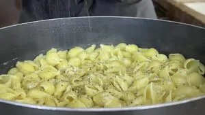 Close-up of pasta shells with black pepper seasoning in a pan.
