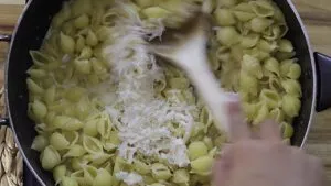 Cooking pasta shells with grated cheese being stirred in a pan with a wooden spoon.
