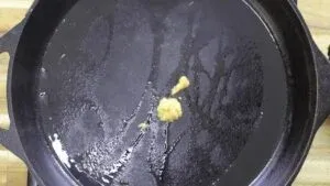 Heating minced garlic in a black skillet, preparing for a flavorful dish.