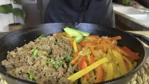 Cast iron skillet with seasoned sliced beef, sautéed bell peppers, and avocado slices.