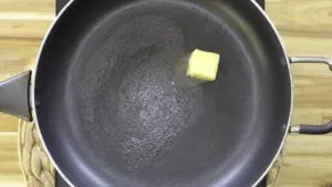 Butter melting in a black frying pan on a wooden countertop, preparing for cooking.
