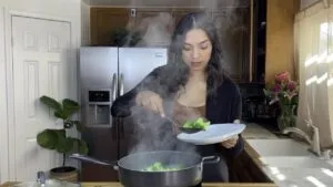 Woman removing steamed broccoli from a pot in a kitchen.