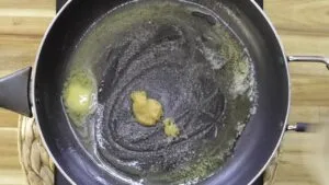 Melting butter and garlic paste sizzling in a black frying pan on a wooden kitchen table.