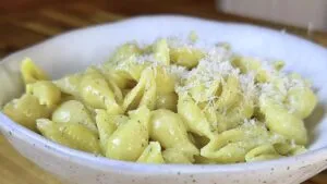 Creamy shell pasta topped with grated cheese in a white bowl on a wooden table.
